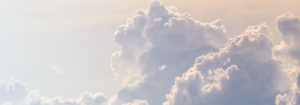 Fluffy white clouds against a soft, light blue sky with a warm, gentle glow from the sunlight.
