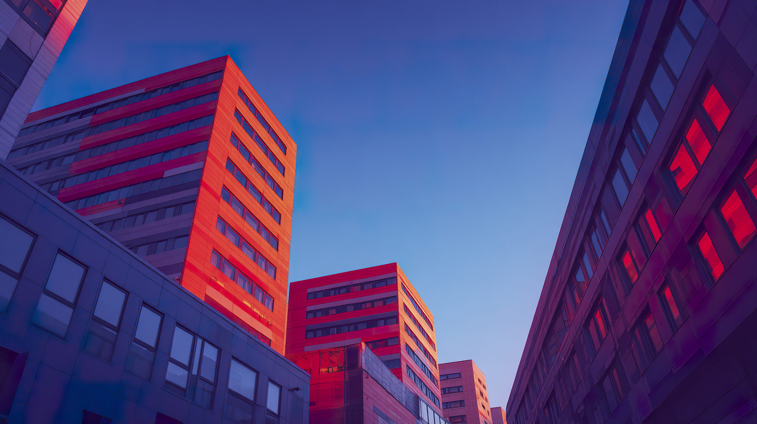 Modern cityscape with tall office buildings reflecting warm sunset light under clear blue sky, showcasing urban architecture and vibrant colors in peaceful evening atmosphere
